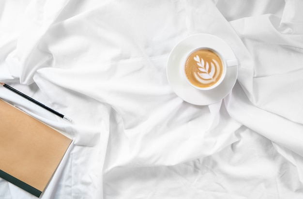 Cup of coffee in bed. Morning flatlay in white bed. Cappuccino and morning routine. The beginning of the day