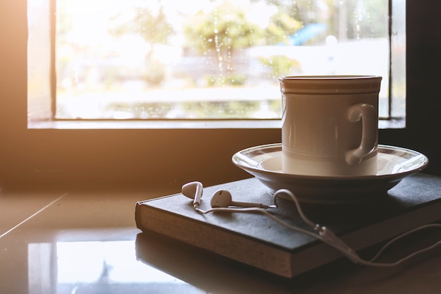 Cup of coffee on book by the window on a rainy day with soft-focus in the background. 