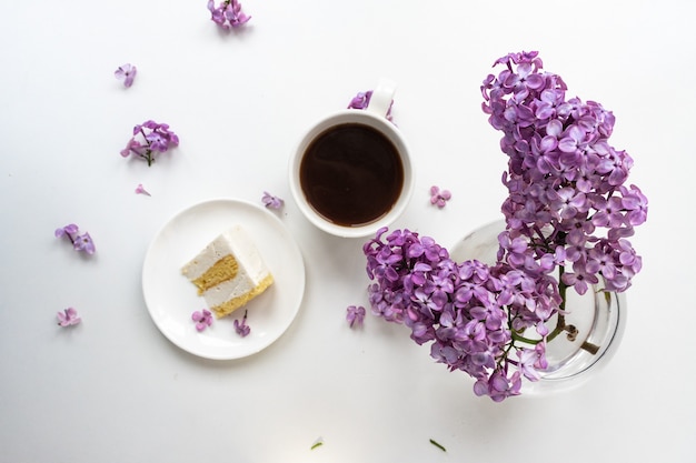 Cup of coffee and cake horns fromstill life with a bouquet of lilacs on a white table, a cup of coffee, a plate with a piece of cake. international Women's Day, March 8