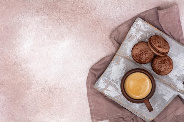 A cup of coffee and chocolate macarons on a wooden board View from above Breakfast concept