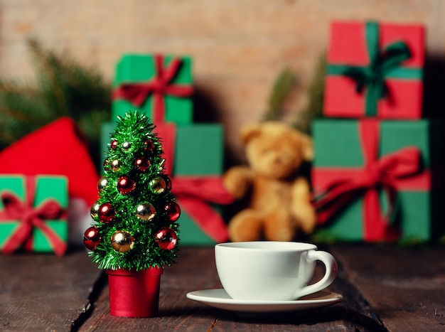 Cup of coffee and Christmas tree next to gifts on wooden table