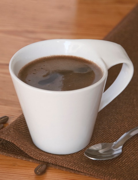 A cup of coffee close-up next to teaspoon and roasted coffee beans.