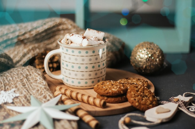 Cup of coffee or cocoa with marshmallows, cinnamon sticks, knitted plaid and Christmas toys. 