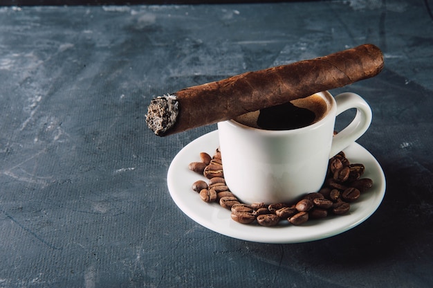 Cup of coffee, coffee beans, ashtray with cigar on dark