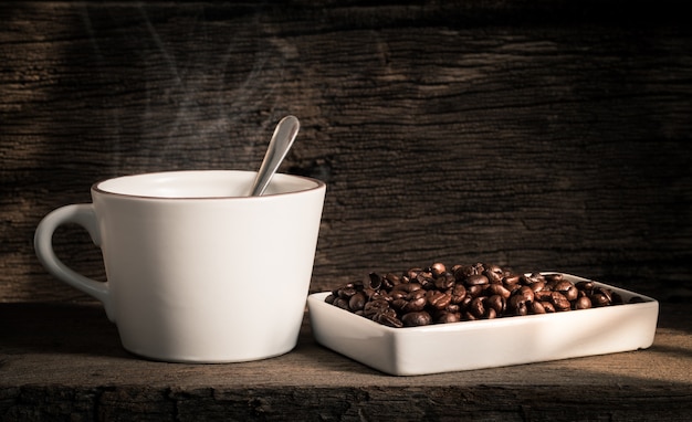 A cup of coffee and coffee beans on an old wooden table.