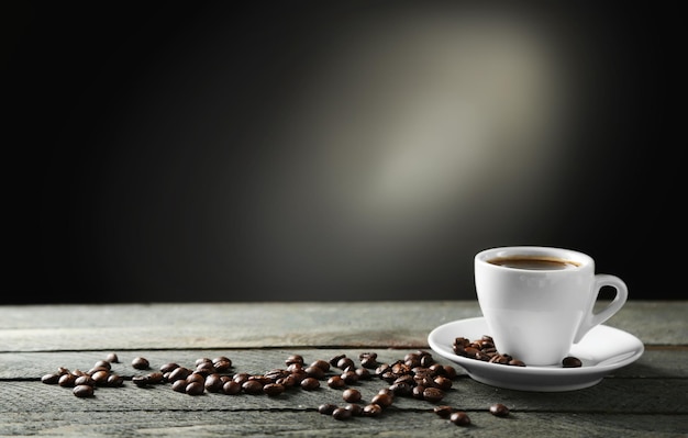 Cup of coffee and coffee grains on wooden table on gray background