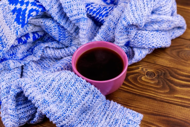 Cup of coffee and cozy knitted sweater on wooden table