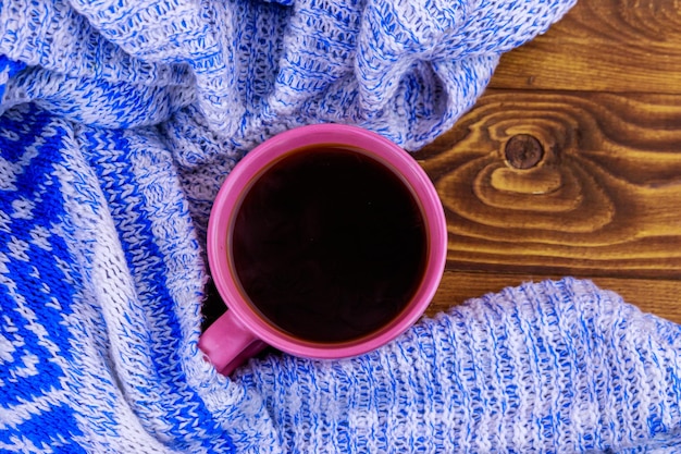 Cup of coffee and cozy knitted sweater on wooden table