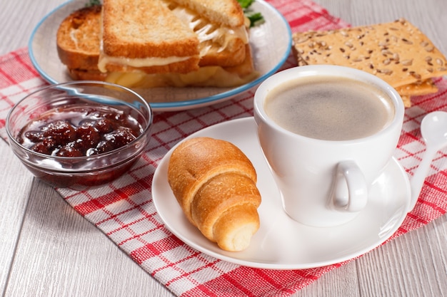 cup of coffee and croissant on saucer glass bowl with strawberry jam cookies