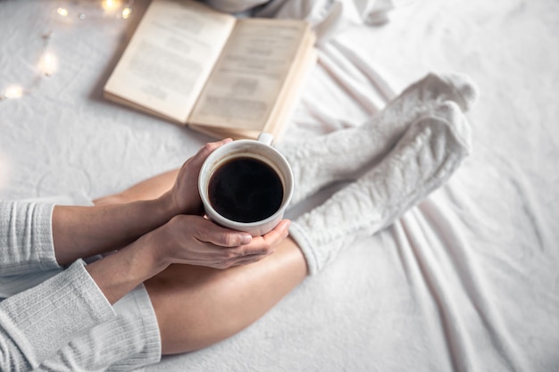 Cup of coffee in female hands in bed top view