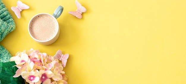 Cup of coffee flowers and knitted element on yellow background flat lay