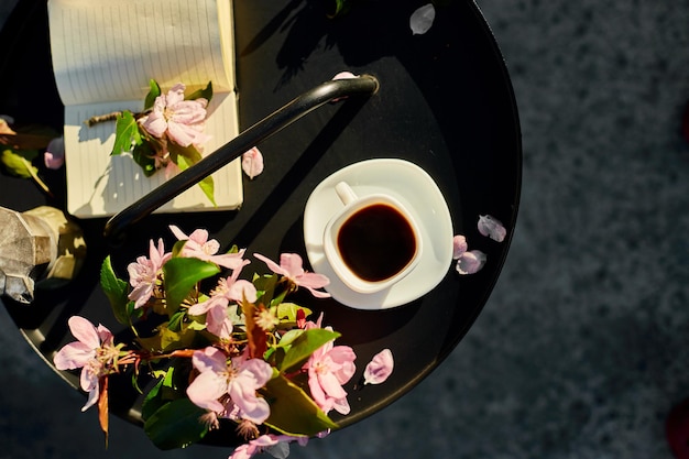 Cup of coffee flowers and notebook on the small black table