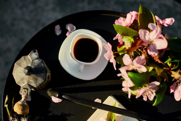 Cup of coffee flowers and notebook on the small black table