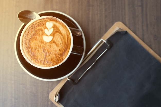 Cup of coffee from above, flat lay image, with paper note on wooden table.