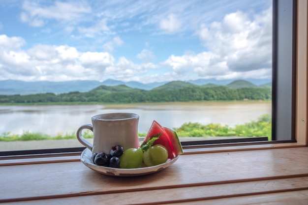 A cup of coffee and a fruit on a plate in front of a window.