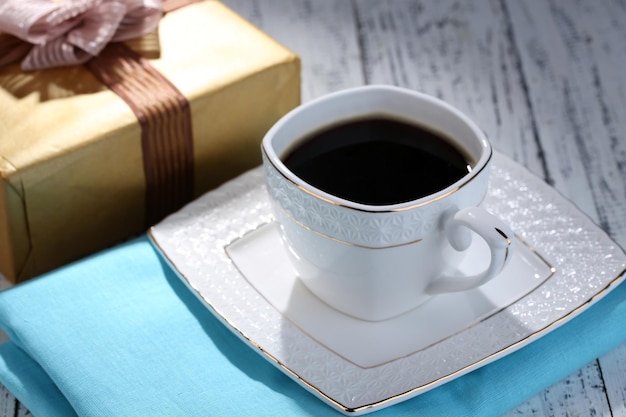 Cup of coffee and gift on wooden table close-up