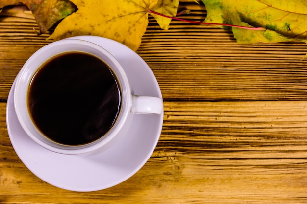 Cup of coffee and heap of yellow maple leaves on a wooden table Top view