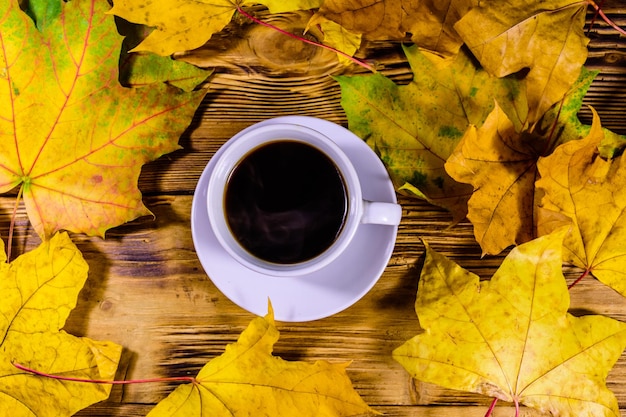 Cup of coffee and heap of yellow maple leaves on a wooden table Top view