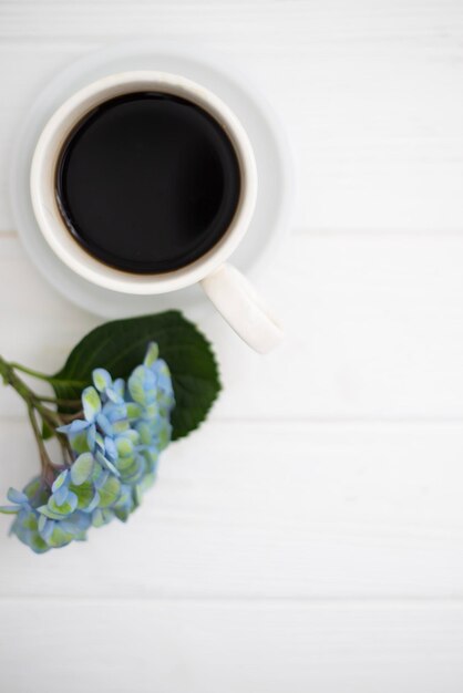 Photo a cup of coffee and hydrangea flowers on a white wooden background