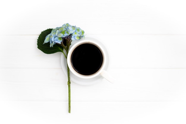 Photo a cup of coffee and hydrangea flowers on a white wooden background