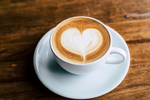 Cup of coffee latte with heart shape on old wooden background in the morning sunlight