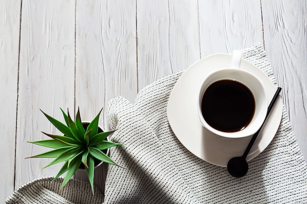 A cup of coffee a light napkin and a succulent plant in a white pot on a light table