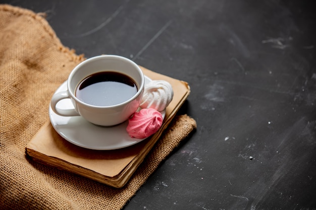 Cup of coffee, meringue and vintage book on a dark table