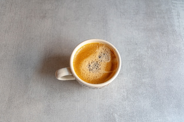 A cup of coffee in the morning light with an appetizing froth on a ceramic gray surface