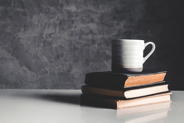 A cup of coffee near of stack of books on grey background