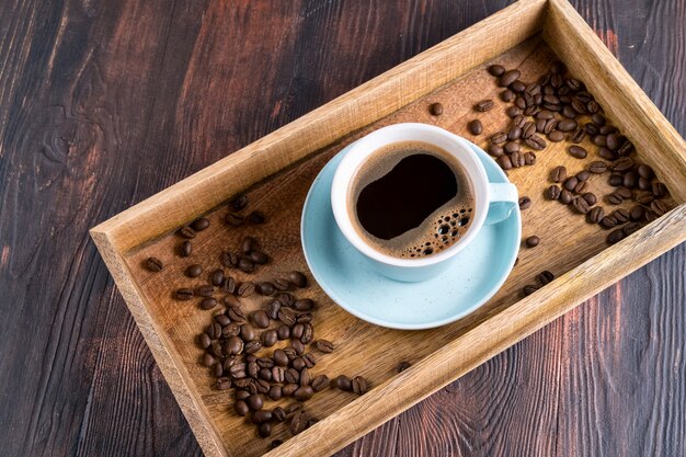 Cup of coffee and nearby coffee beans in a wooden box on a dark wooden