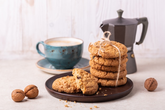 Cup of coffee, oatmeal cookies, coffee maker on white wooden background.