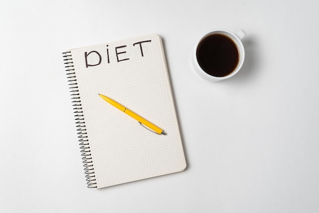 Cup of coffee pen and a notebook title Diet White background directly above