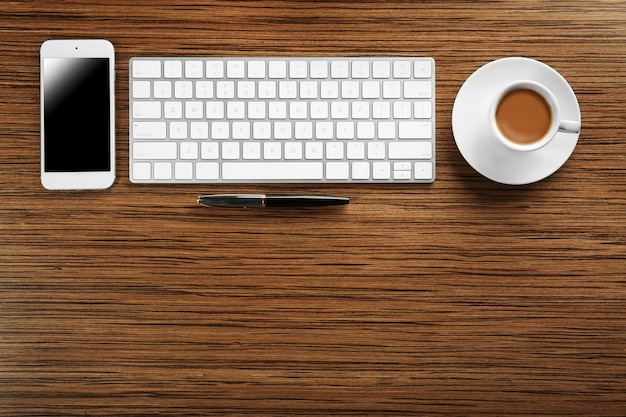 Cup of coffee phone and keyboard on wooden table