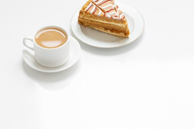 Cup of coffee and piece of cake on white table