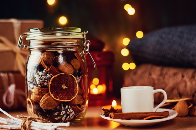 Cup of coffee, pine cones, dried oranges and garland lights on a dark background. 