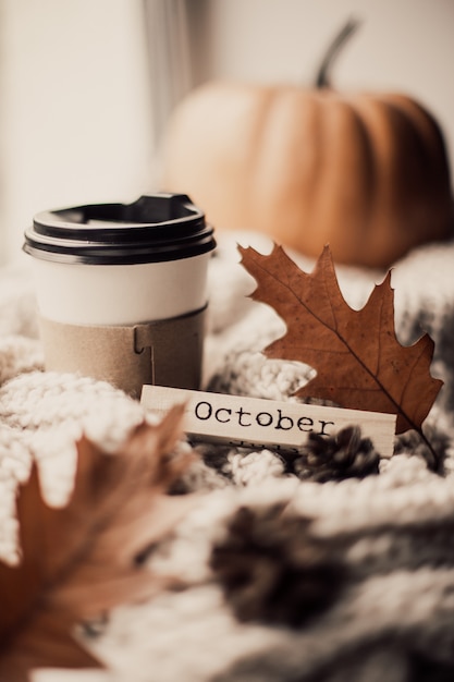 Cup of coffee, pumpkin, dried autumn leaves on window.