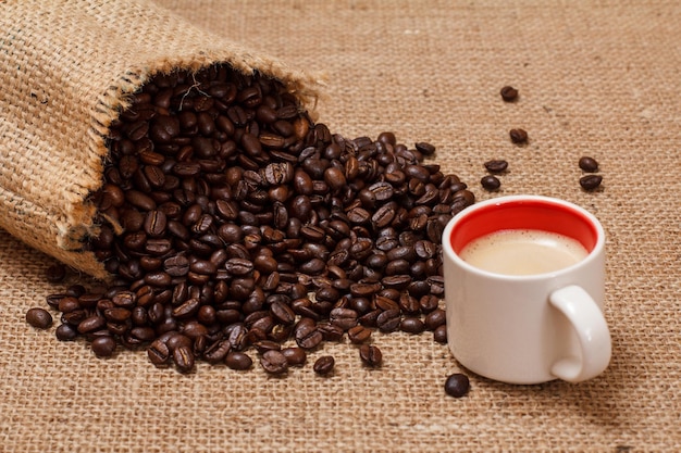 Cup of coffee and roasted coffee beans in a canvas sack on sackcloth background.