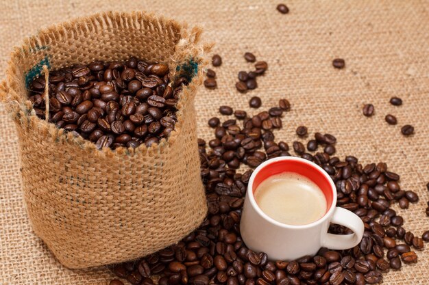 Cup of coffee and roasted coffee beans in a canvas sack on sackcloth. Top view.