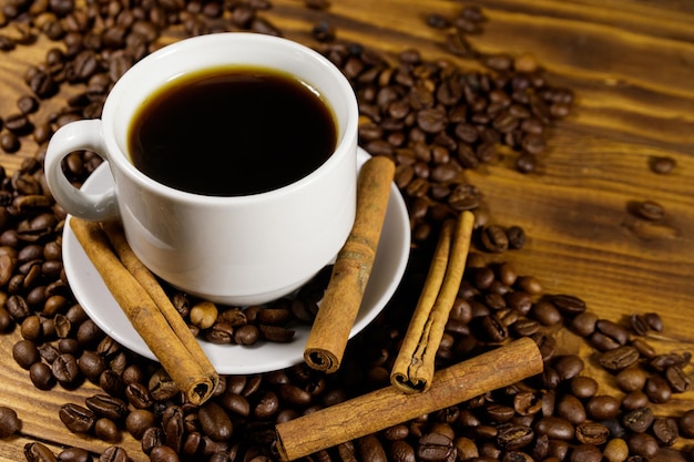 Cup of coffee, roasted coffee beans and cinnamon sticks on wooden table