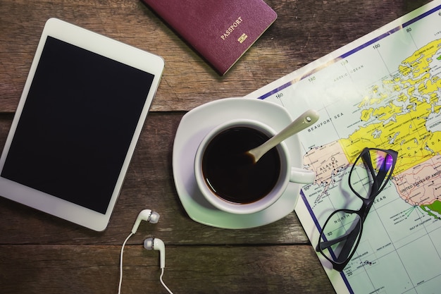 Cup of coffee on rustic wood with ipad and passport and clock and map