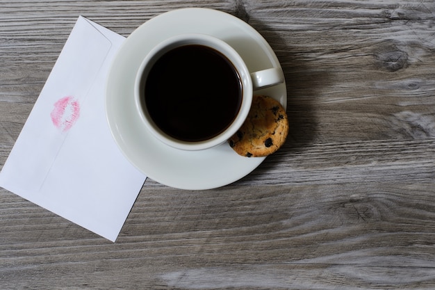 Cup of coffee on saucer with chocolate cookie white envelope with lip print