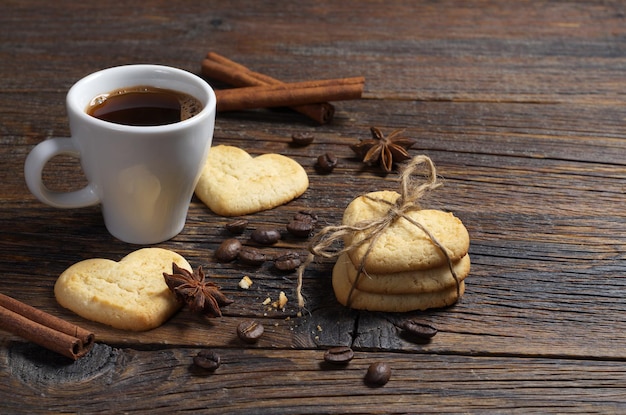 Cup of coffee and shortbread cookies in the shape of a heart on dark wooden table