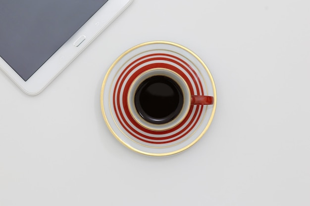 A cup of coffee sits on a table next to a phone and a white tablet.