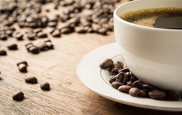 A cup of coffee sits on a table with coffee beans scattered around.