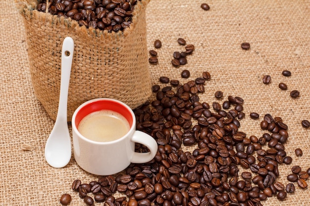 Cup of coffee spoon and roasted coffee beans in a canvas sack on sackcloth Top view