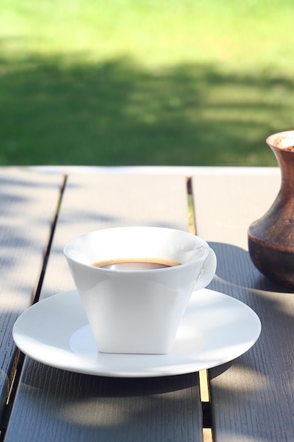 A cup of coffee stands on a wooden table in the garden Behind is a Turk with freshly brewed coffee