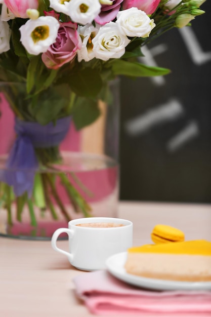 Cup of coffee tasty cake and beautiful bouquet of flowers in cafe