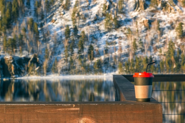 A cup for coffee or tea on the railing on the winter promenade with a beautiful view