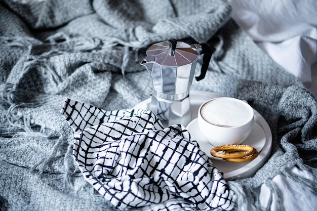 Cup of coffee on tray in cozy winter bad with wool blanket