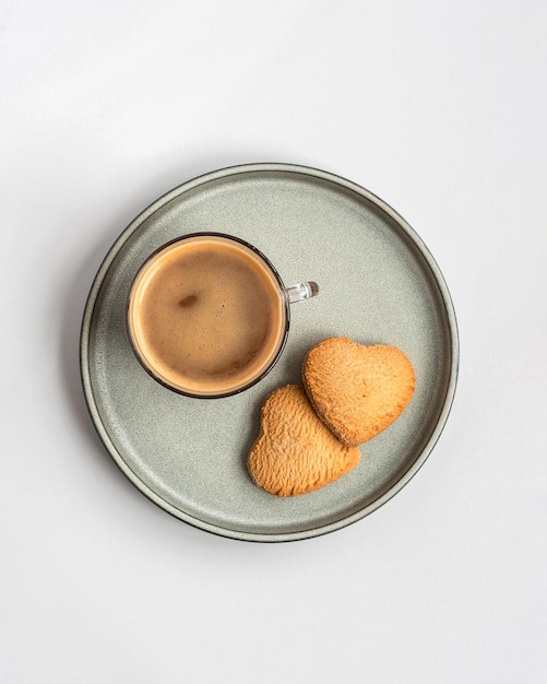 A cup of coffee and two heart shaped cookies in a plate, top view